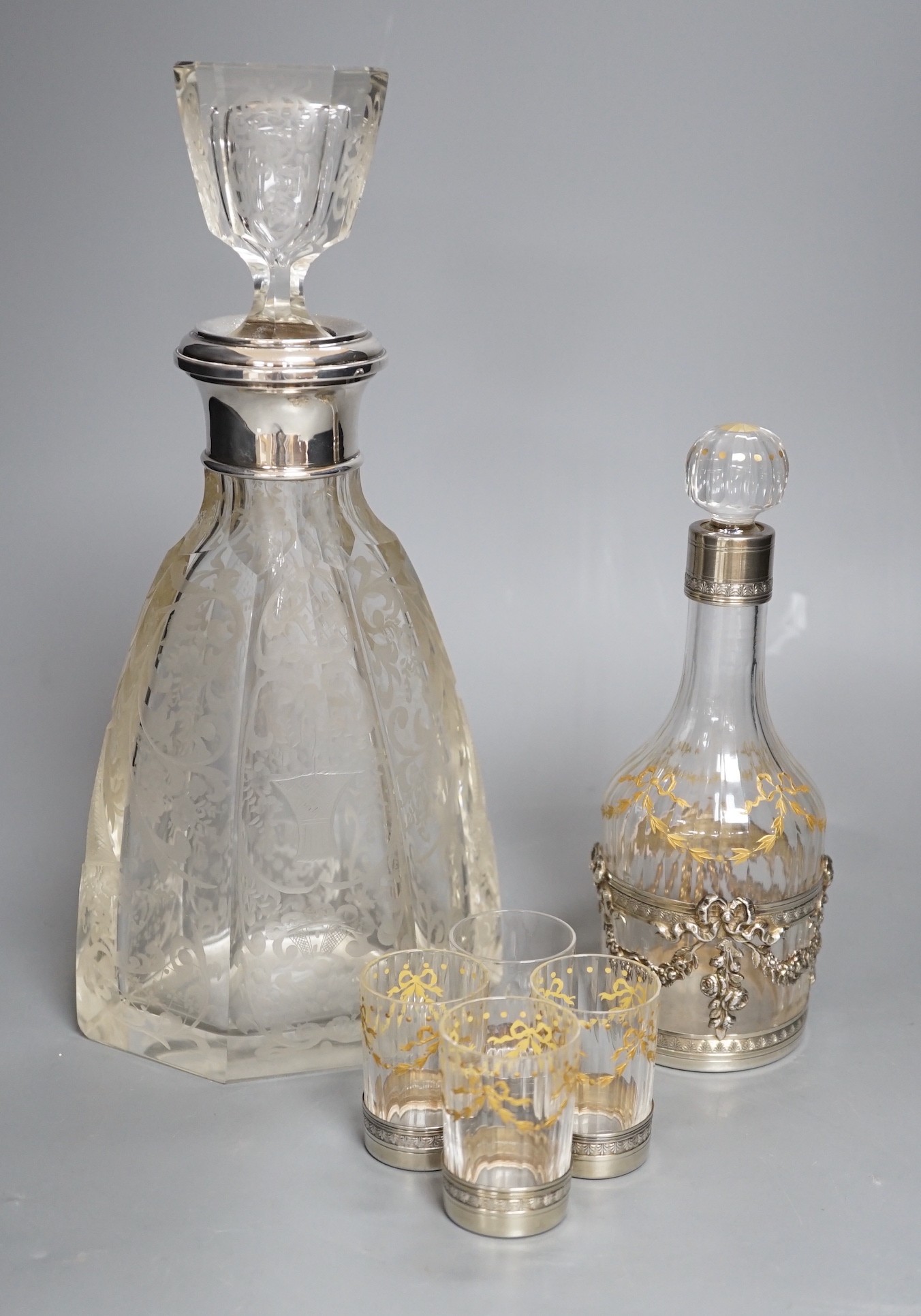 An early 20th century French white metal mounted gilded glass decanter and stopper and four matching tots, decanter height 19.7cm, and a French white metal collared etched glass decanter and stopper.